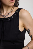 Black slash neck open back tank top with silver eyelet detail, worn by model