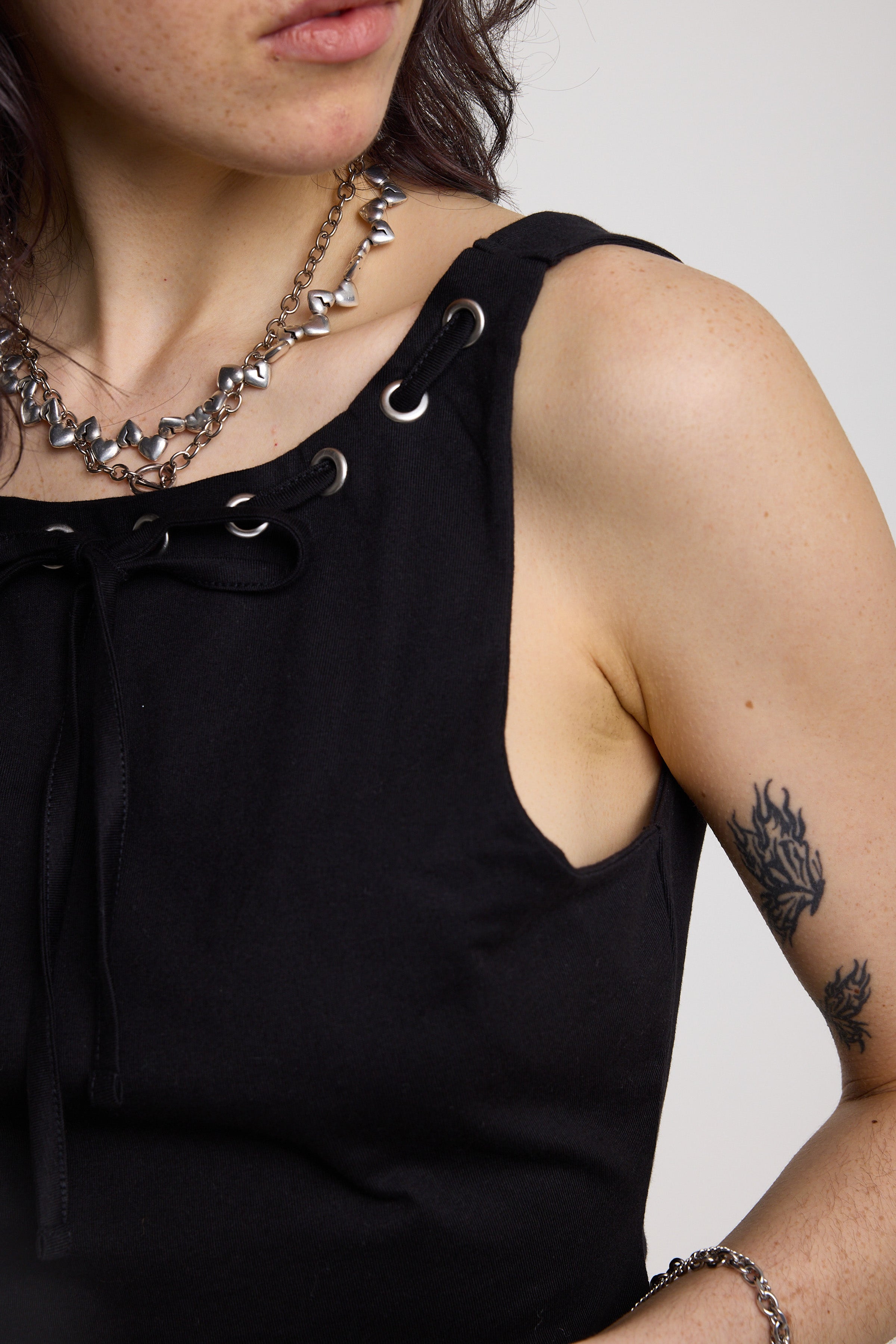 Black slash neck open back tank top with silver eyelet detail, worn by model