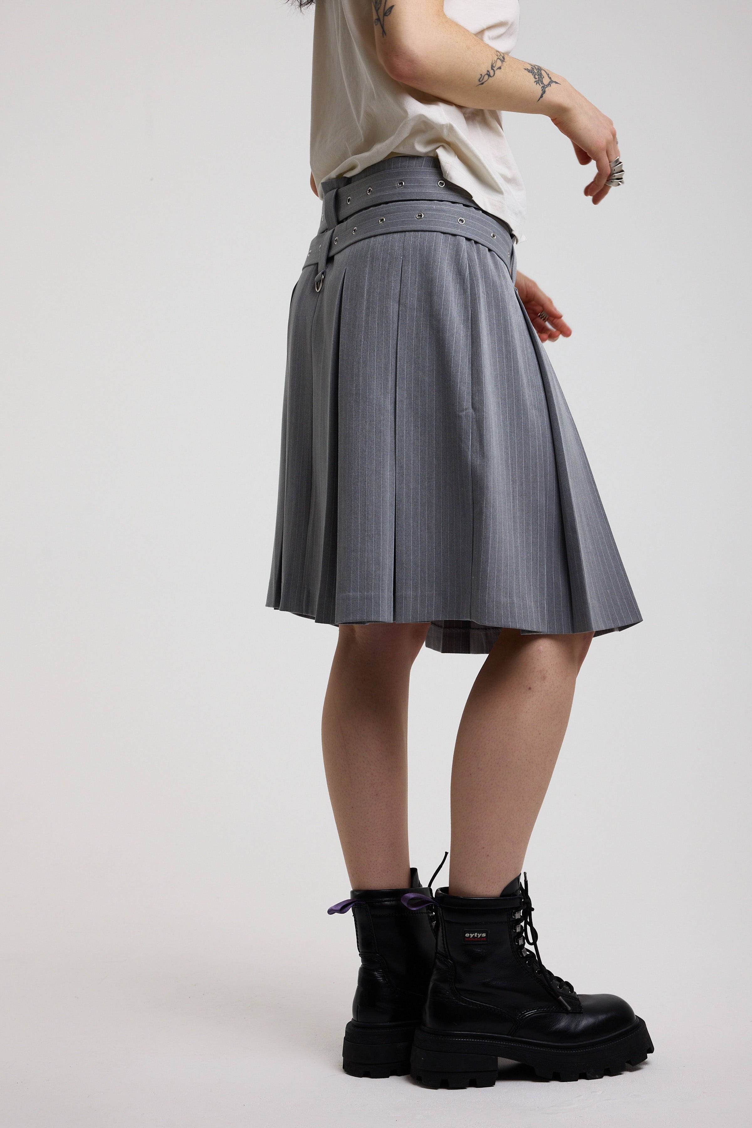 Grey pinstripe pleated midi skirt with eyelet hardware belt and D ring details, worn by model