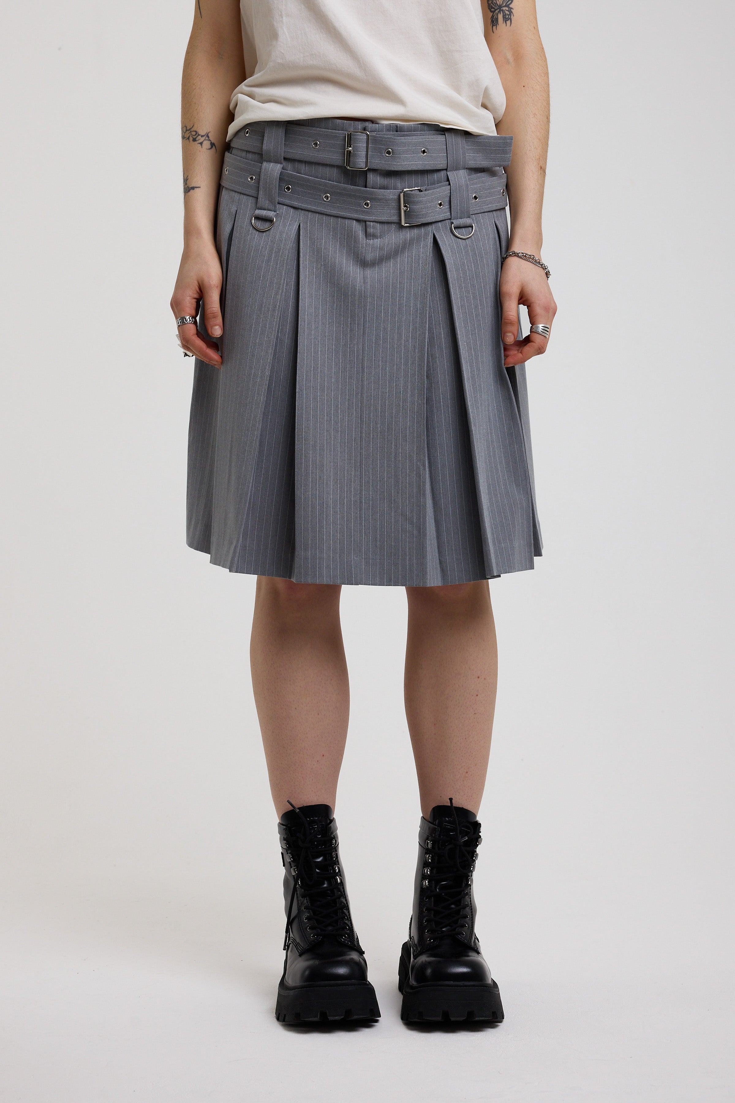 Grey pinstripe pleated midi skirt with eyelet hardware belt and D ring details, worn by model