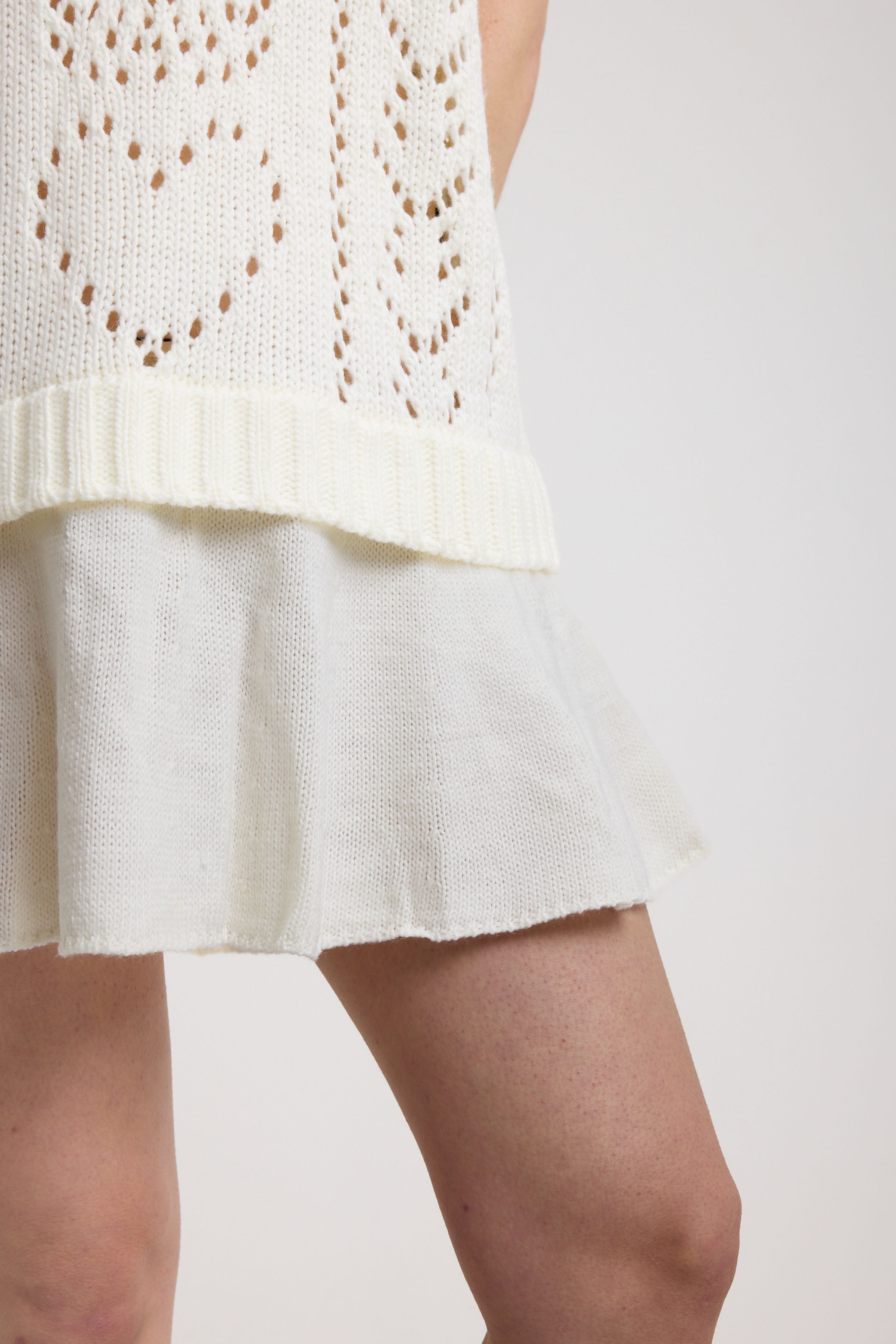 Close up of peplum hem on of-white skull and heart pointelle knit mini dress, worn by model