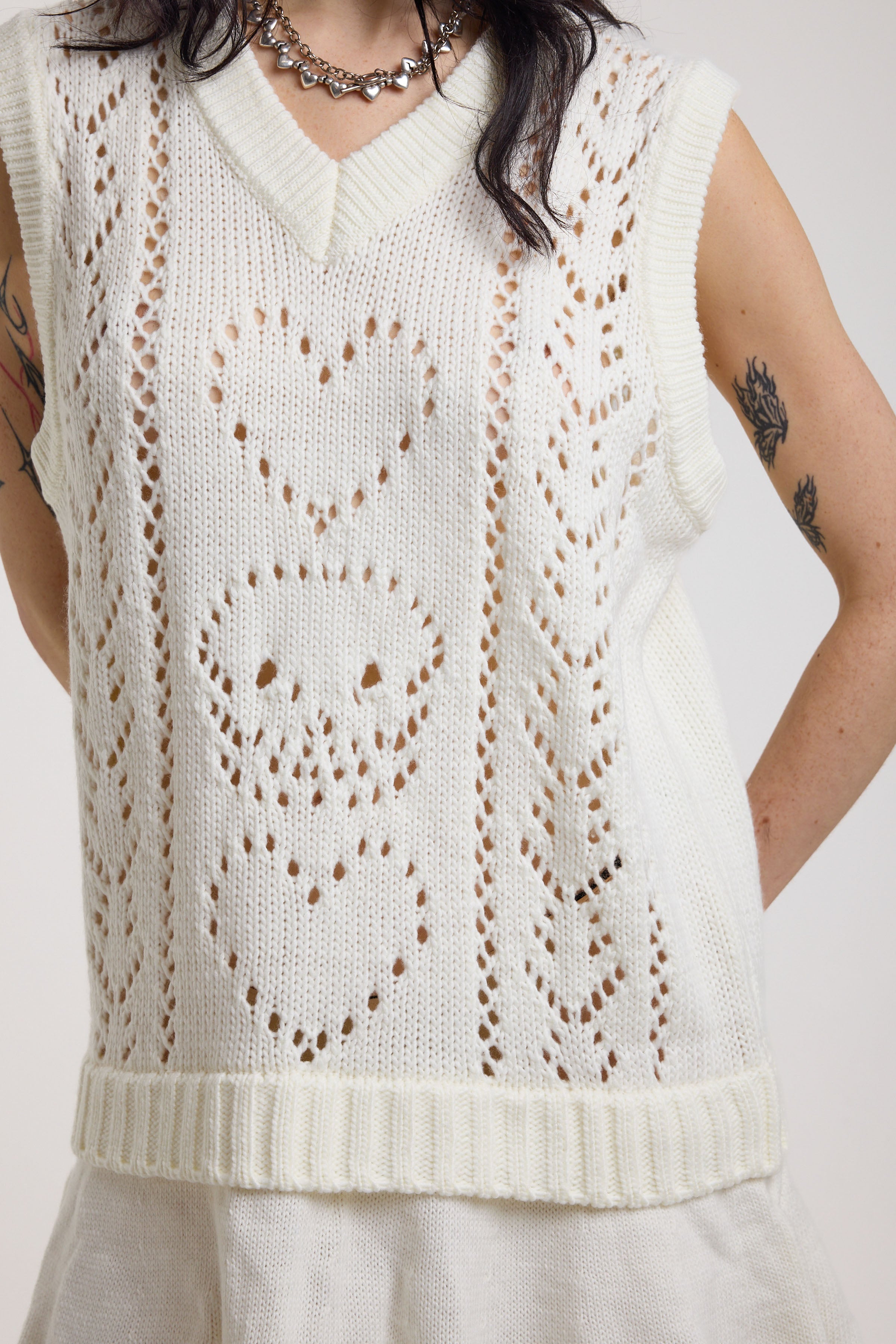 Close up showing skull and heart pointelle detail on off-white knit mini dress with peplum hem, worn by model