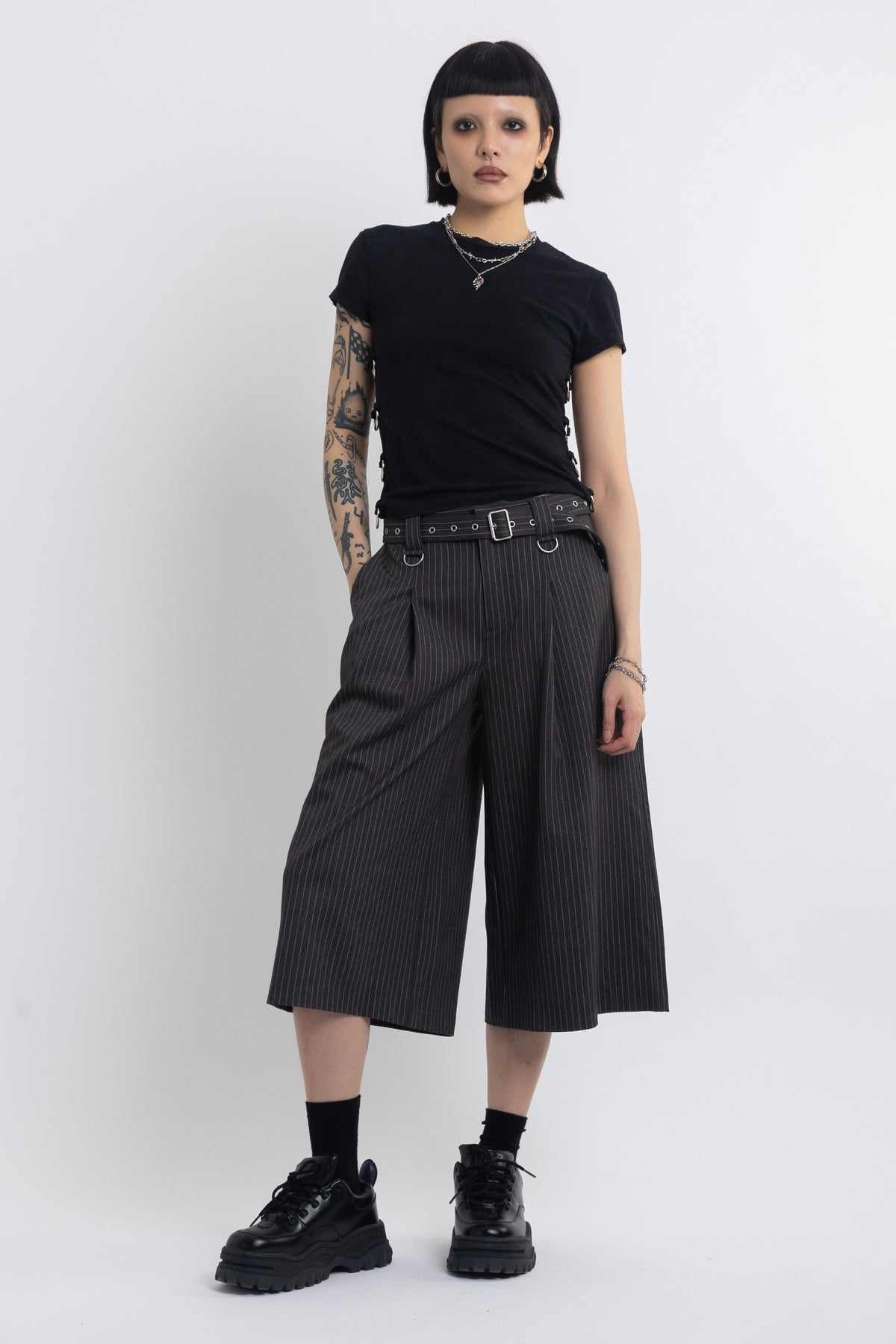 Grey pinstripe longline tailored shorts with eyelet belt and D-ring hardware, worn by model