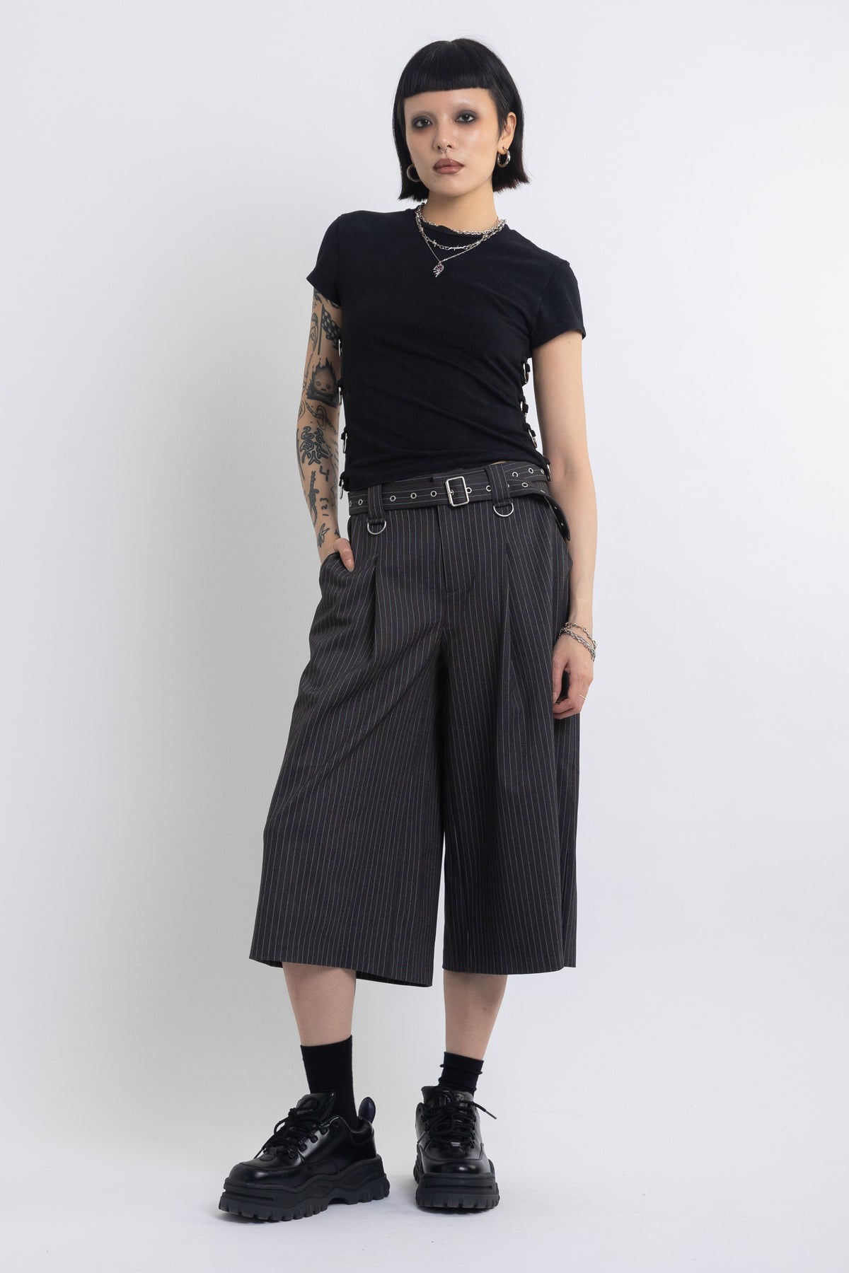 Grey pinstripe longline tailored shorts with eyelet belt and D-ring hardware, worn by model