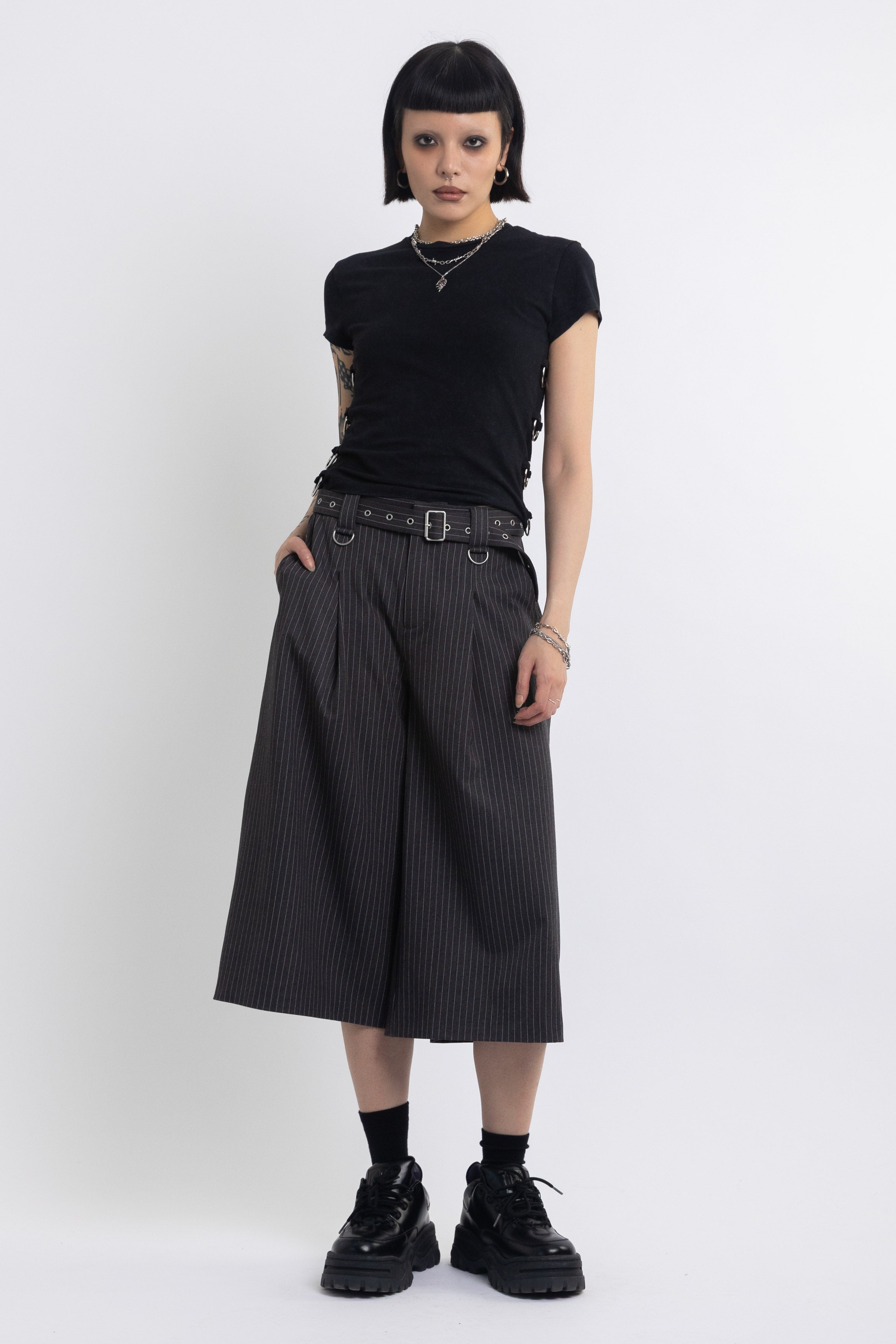 Grey pinstripe longline tailored shorts with eyelet belt and D-ring hardware, worn by model