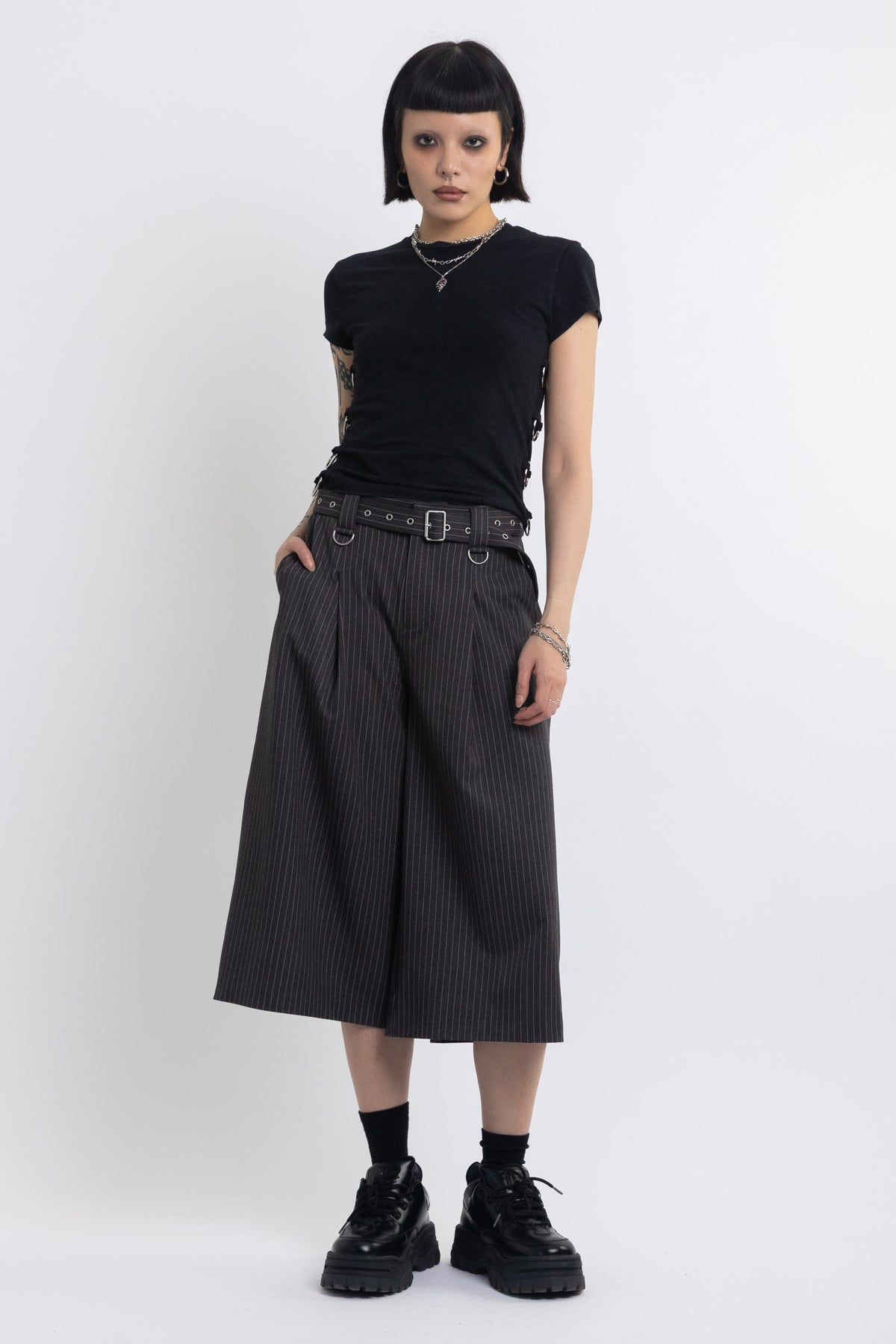 Grey pinstripe longline tailored shorts with eyelet belt and D-ring hardware, worn by model