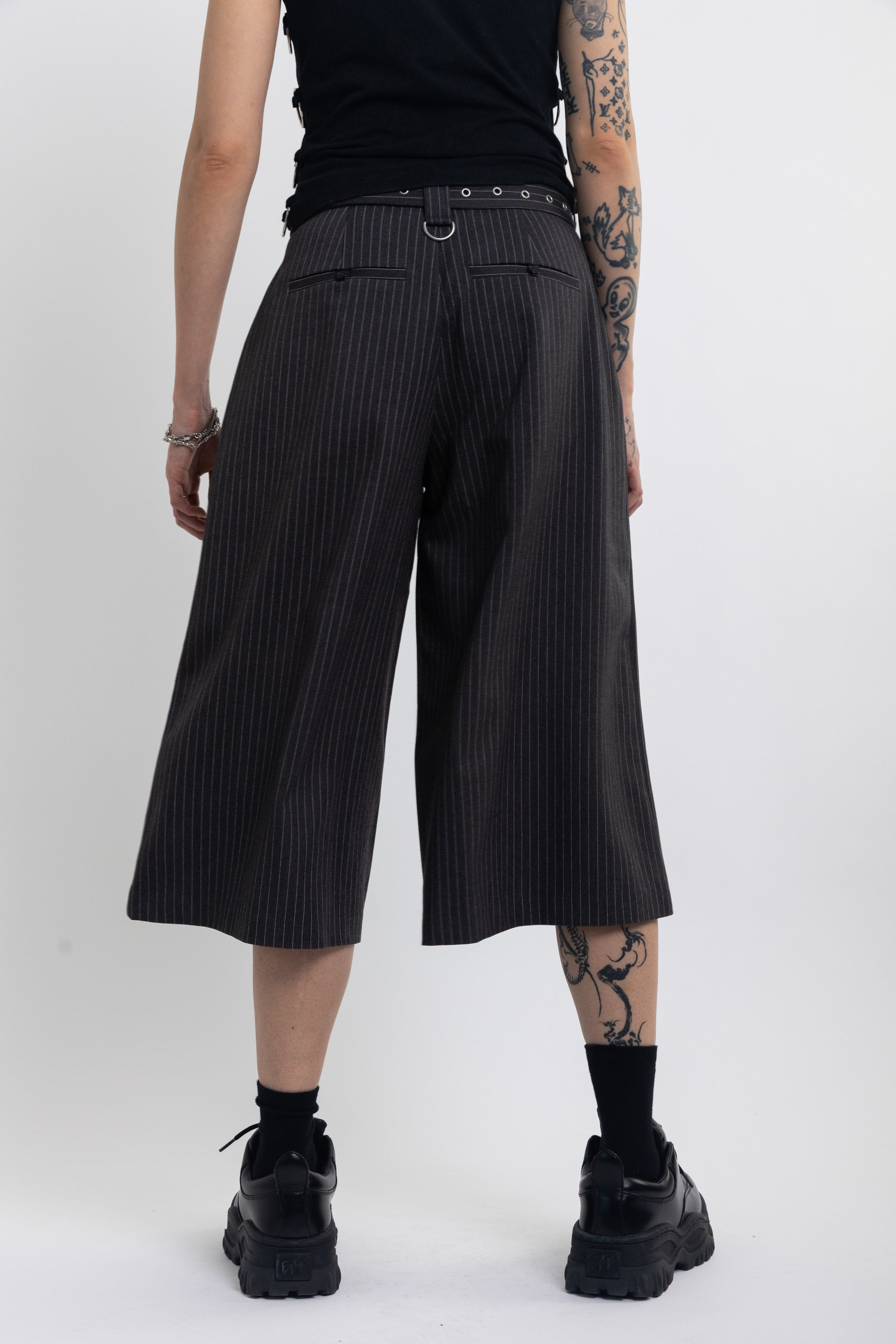 Grey pinstripe longline tailored shorts with eyelet belt and D-ring hardware, worn by model