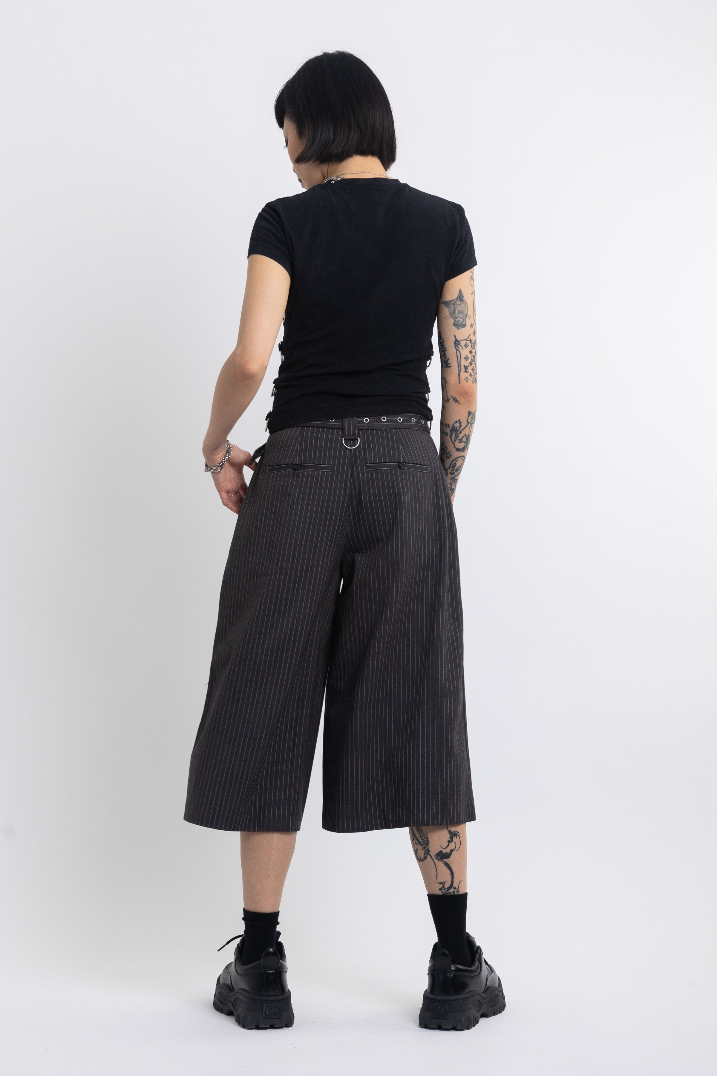 Grey pinstripe longline tailored shorts with eyelet belt and D-ring hardware, worn by model