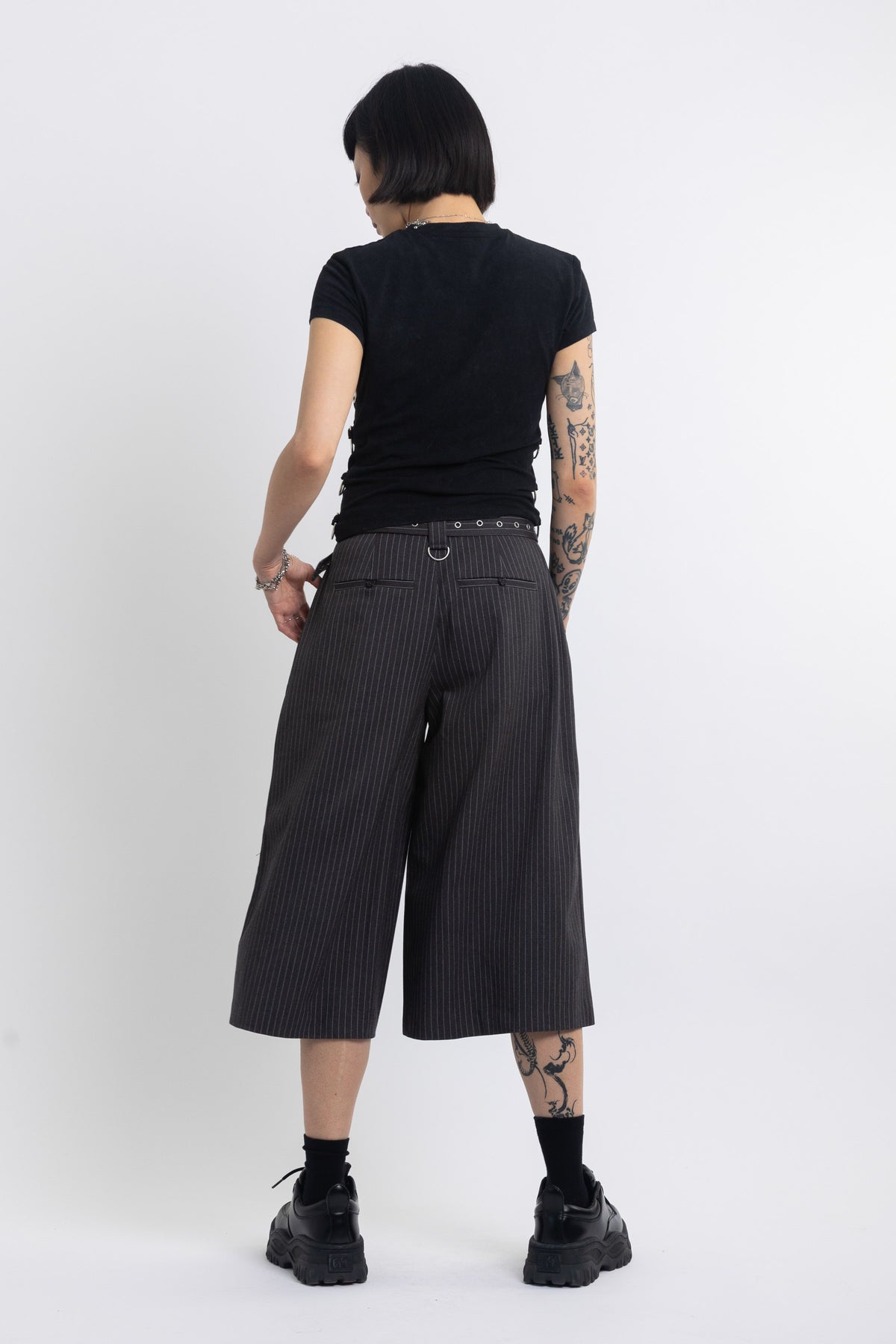 Grey pinstripe longline tailored shorts with eyelet belt and D-ring hardware, worn by model