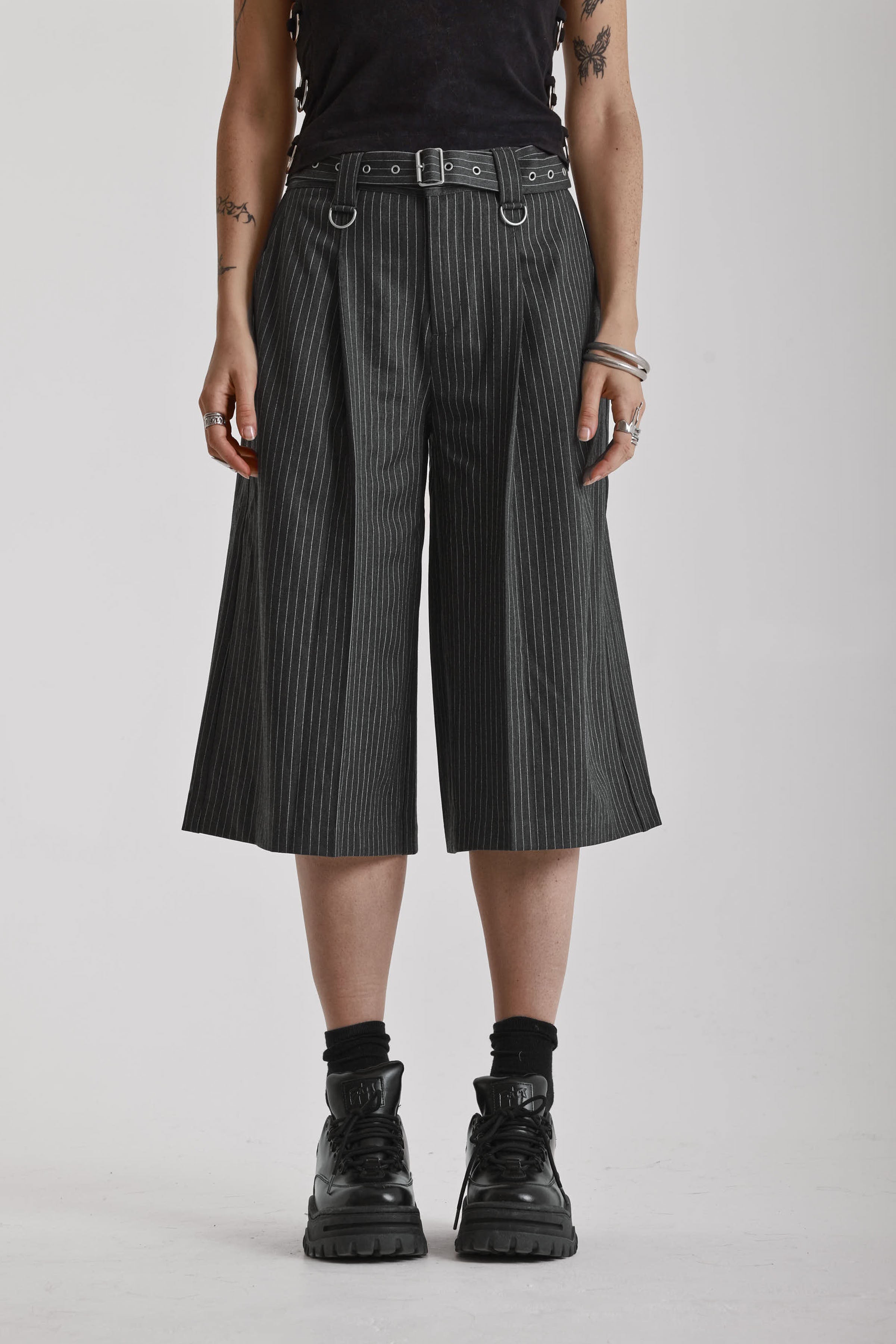 Grey pinstripe longline tailored goliath shorts with silver eyelet belt and D-ring hardware, worn by model