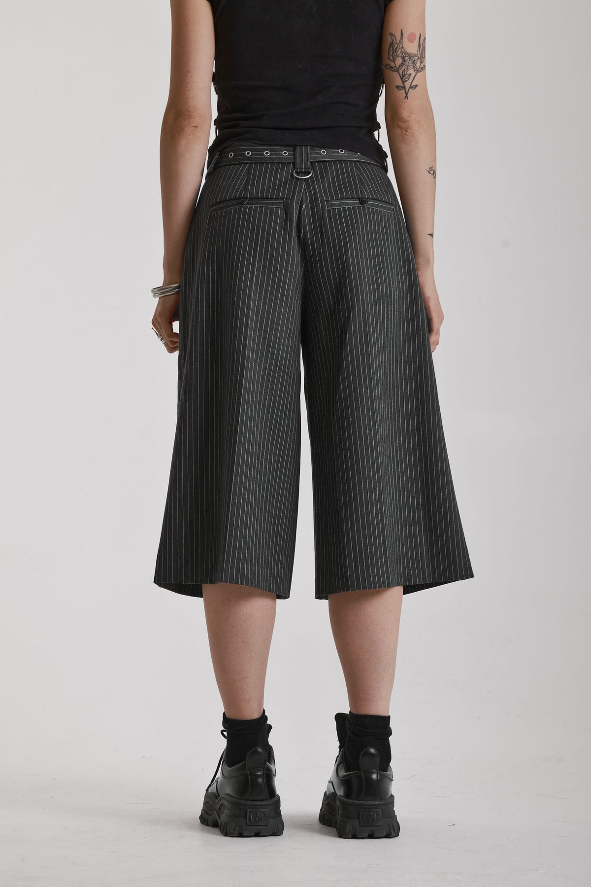 Grey pinstripe longline tailored goliath shorts with silver eyelet belt and D-ring hardware, worn by model