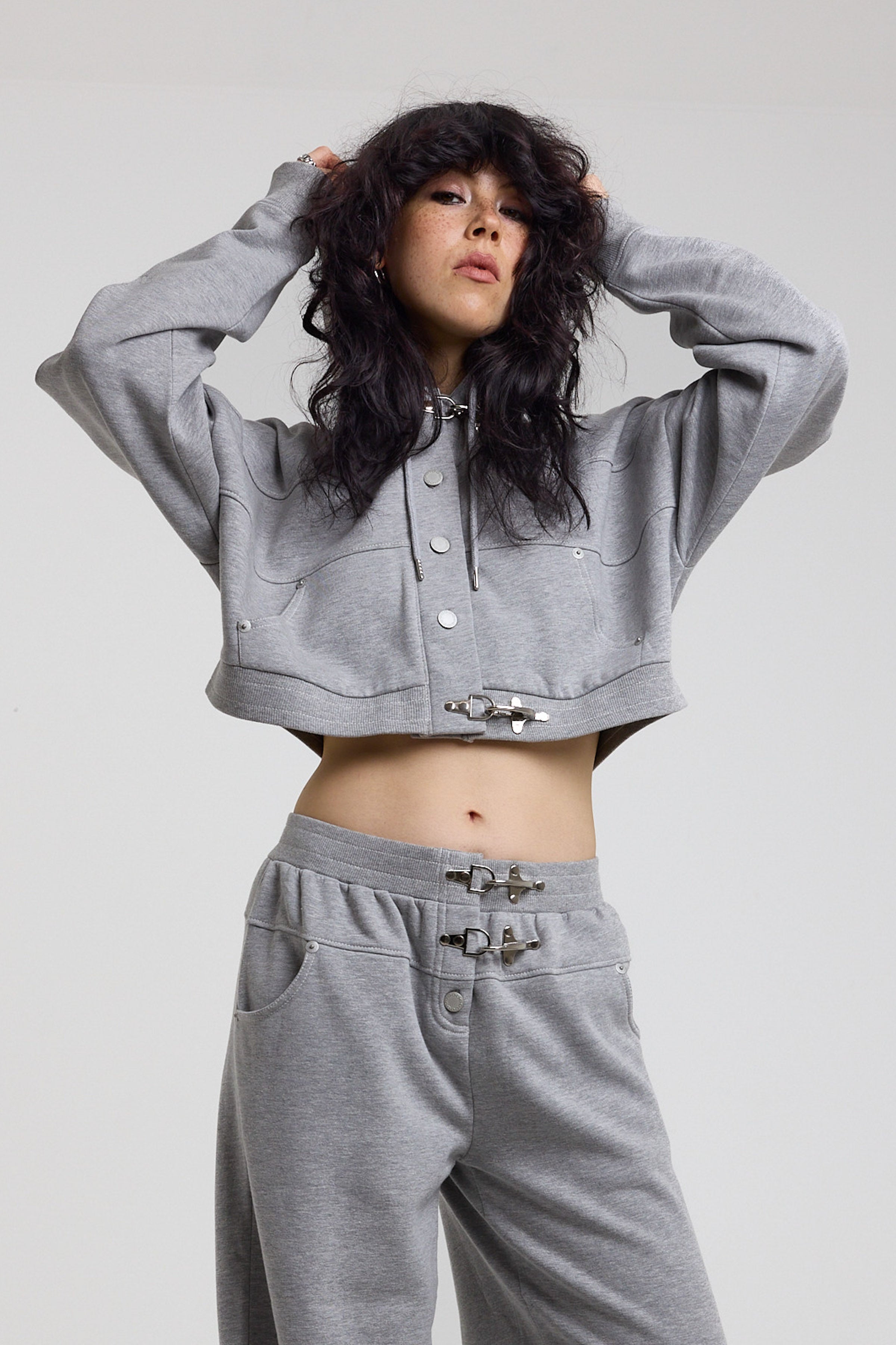 Grey cropped hoodie with silver hardware clasps, worn by model