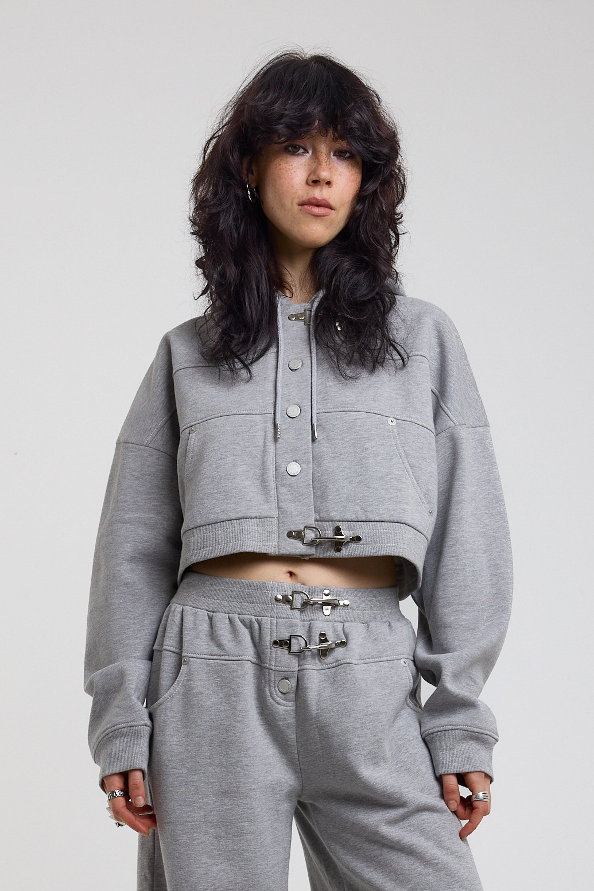 Grey cropped hoodie with silver hardware clasps, worn by model