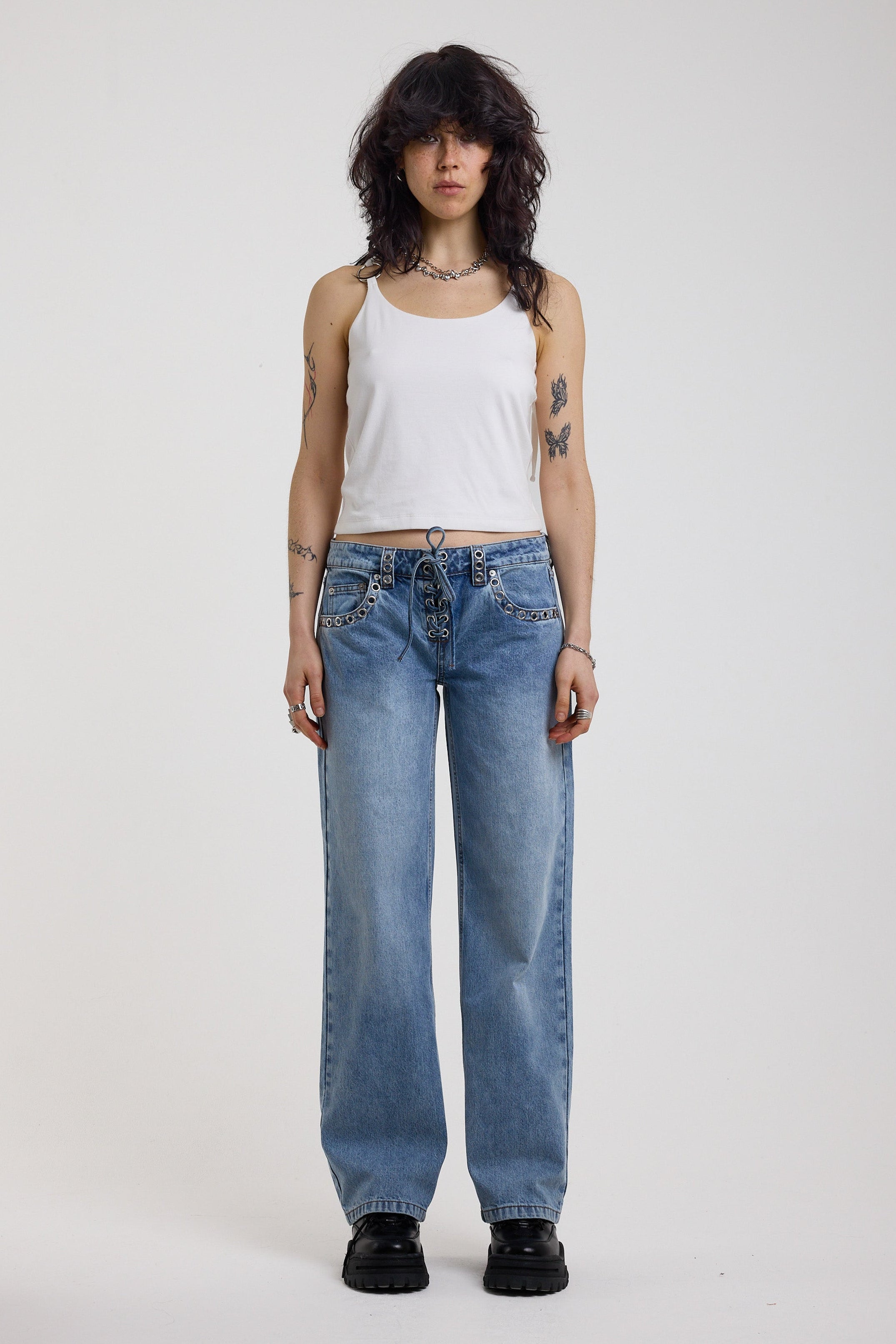 Washed blue denim relaxed straight leg jeans with lace up front and eyelet and rivet hardware, worn by model