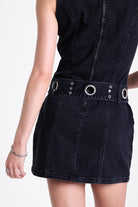 Black denim mini dress with silver trigger clasp eyelet detail belt, worn by model